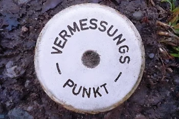 Vermessungsleistung - Grenzvermessung / Amtliche Grenzanzeige Das Bild zeigt einen Vermessungspunkt, der im Erdboden eingelassen ist